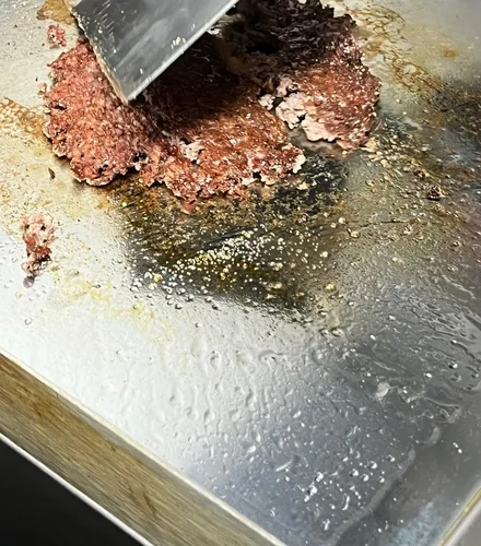 A smash patty being pressed onto the hot griddle